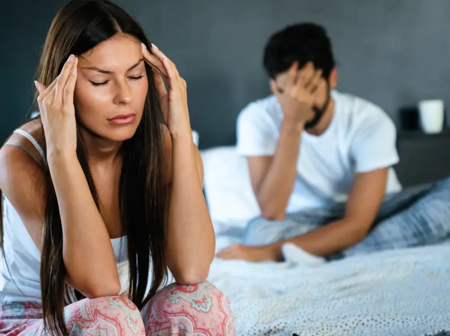 Man and women sitting on the bed with their hands over their face and on temple expressing sexual frustration