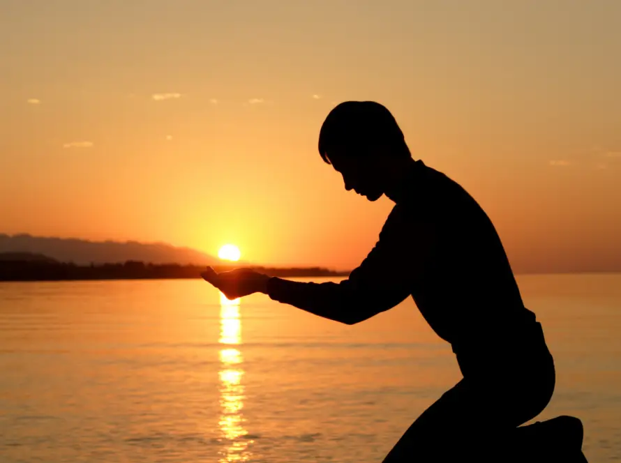 shadow of a person kneeling in front of the sunset, cuppping their hands so it looks like they are holding the sun. This is to portray peace and acceptance